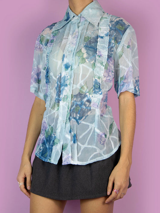 The Y2K Print Sheer Blouse is a vintage 2000s boho summer style light blue floral graphic semi-transparent short-sleeve top with a collar, buttons, and gathered ruffle details.