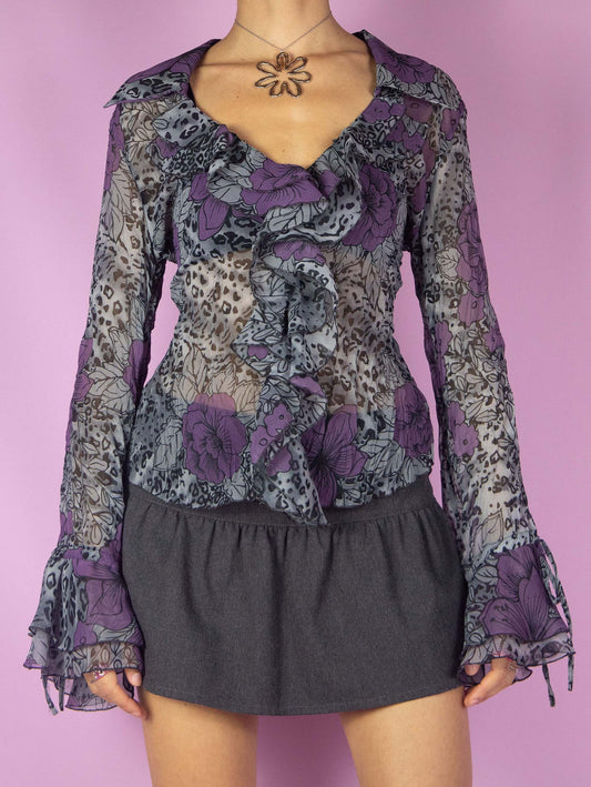 The Y2K Print Sheer Ruffle Blouse is a vintage 2000s top featuring a floral and leopard animal print, long bell sleeves, and a ruffle front. This semi-transparent blouse with frill details adds a touch of whimsy making it perfect for any statement outfit.