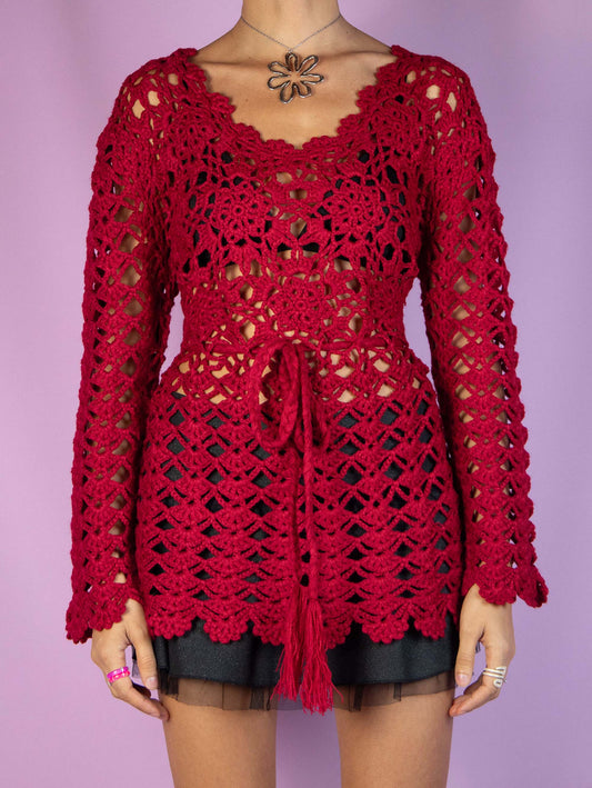 The Y2K Red Crochet Knit Top is a vintage 2000s romantic boho-style crocheted pullover that ties at the waist, crafted from a warm wool blend. Ideal as a chic sweater for everyday casual looks or as a festive addition to any party wardrobe. Excellent vintage condition.