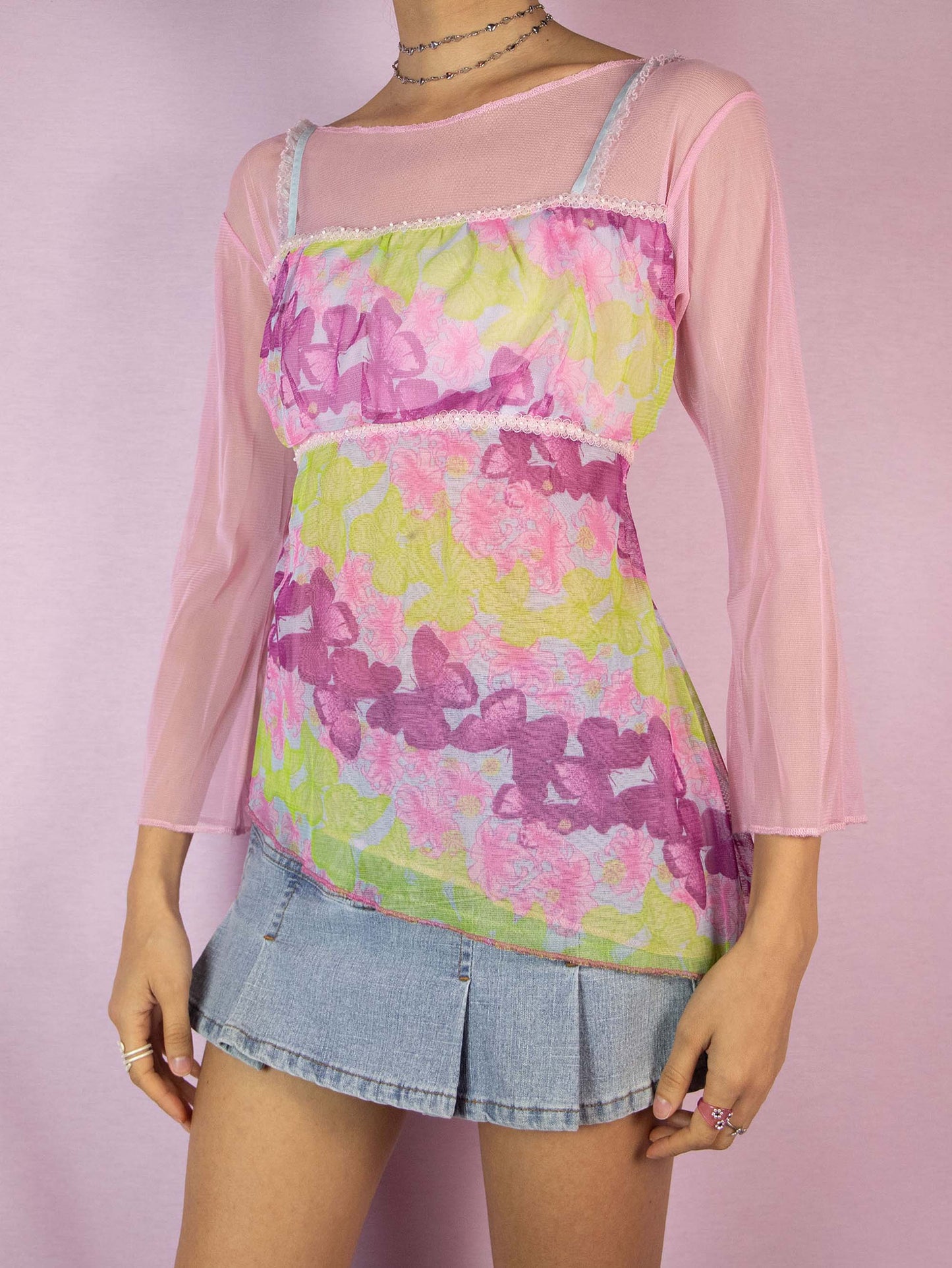 The Y2K Pink Printed Mesh Top is a vintage 2000s romantic fairy cottagecore light pink and green semi-sheer top with floral and butterfly graphics, three-quarter sleeves, and an asymmetric hem. Excellent vintage condition.