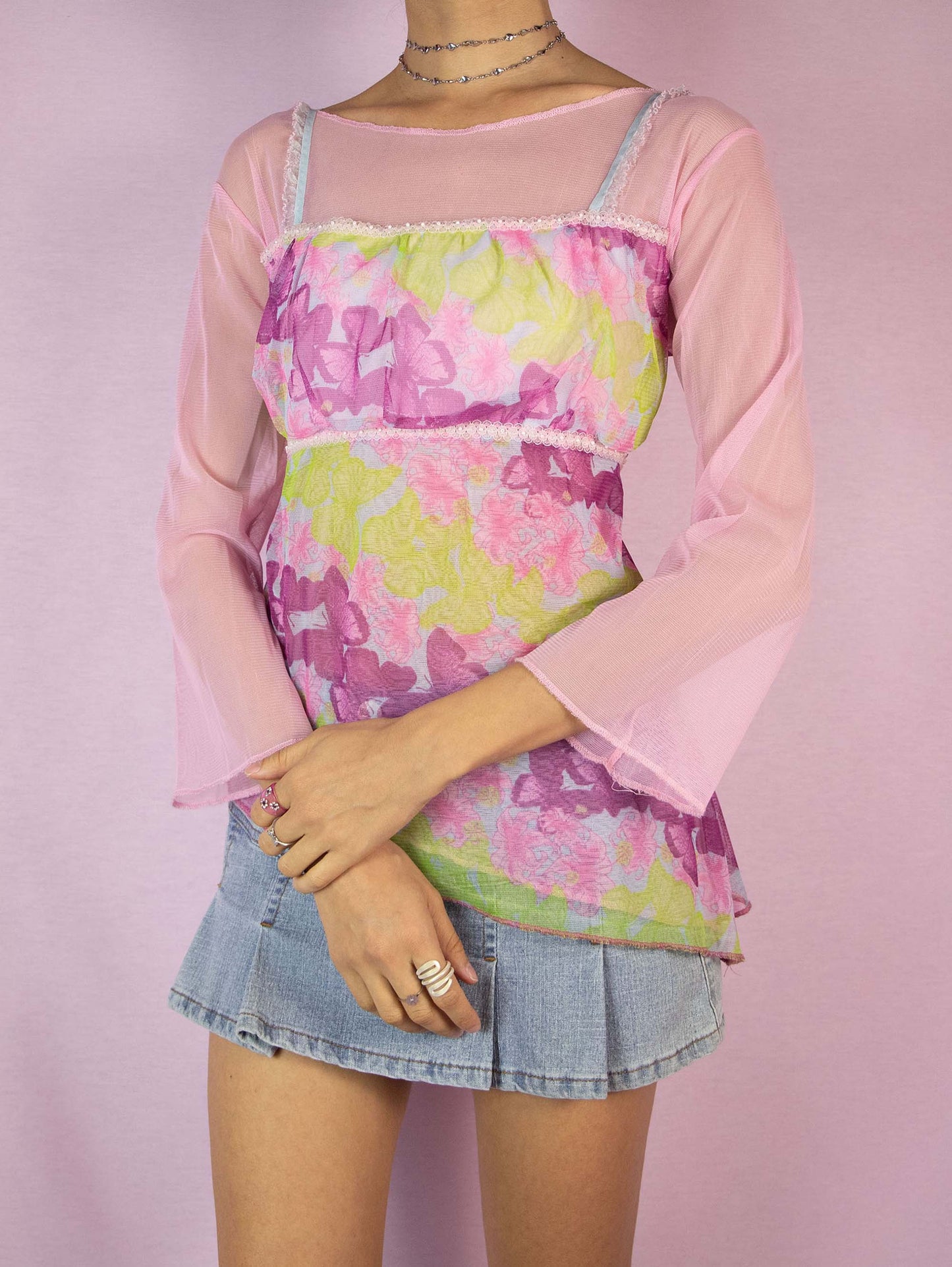 The Y2K Pink Printed Mesh Top is a vintage 2000s romantic fairy cottagecore light pink and green semi-sheer top with floral and butterfly graphics, three-quarter sleeves, and an asymmetric hem. Excellent vintage condition.