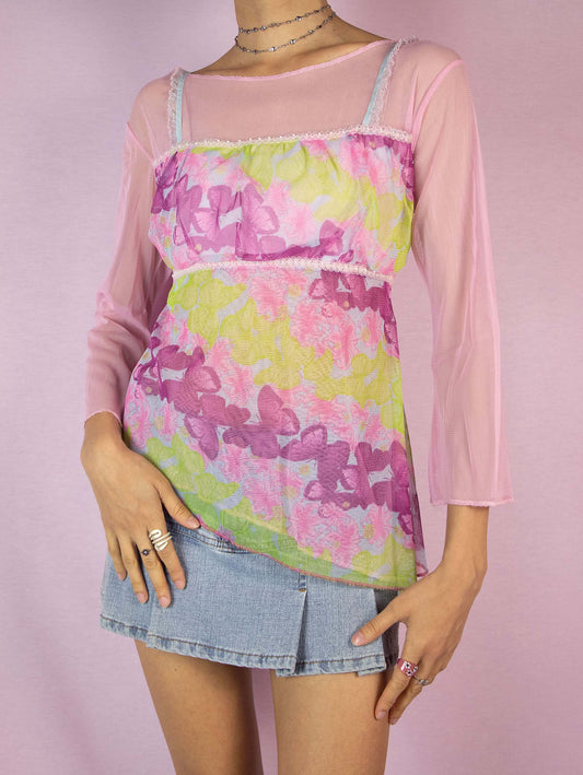 The Y2K Pink Printed Mesh Top is a vintage 2000s romantic semi-sheer top in light pink and green, adorned with whimsical floral and butterfly graphics. Featuring three-quarter sleeves and an asymmetric hem, this enchanting piece adds a fairy-like and playful touch to any party or special event ensemble. Excellent vintage condition.