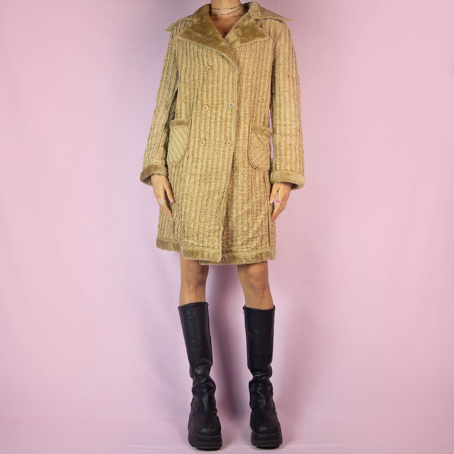 The Y2K Beige Faux Fur Long Coat is a vintage 2000s piece featuring a textured ribbed exterior with a plush faux fur lining throughout. This casual overcoat has a double-breasted button closure, faux fur-trimmed collar, cuffs, and hem, as well as front pockets. Perfect for keeping cozy during casual winter outings.