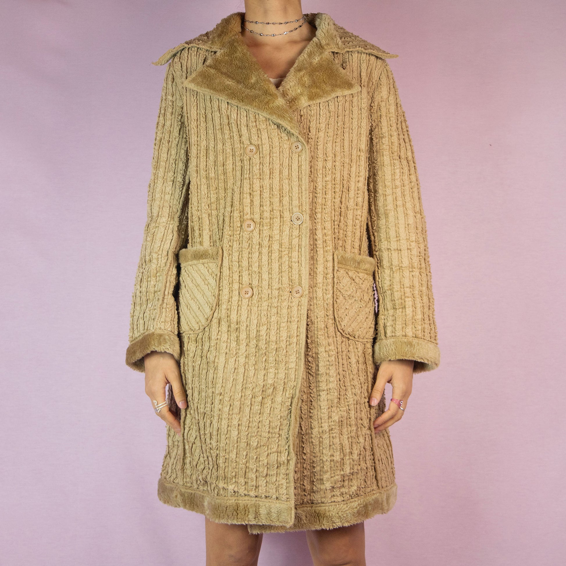 The Y2K Beige Faux Fur Long Coat is a vintage 2000s piece featuring a textured ribbed exterior with a plush faux fur lining throughout. This casual overcoat has a double-breasted button closure, faux fur-trimmed collar, cuffs, and hem, as well as front pockets. Perfect for keeping cozy during casual winter outings.