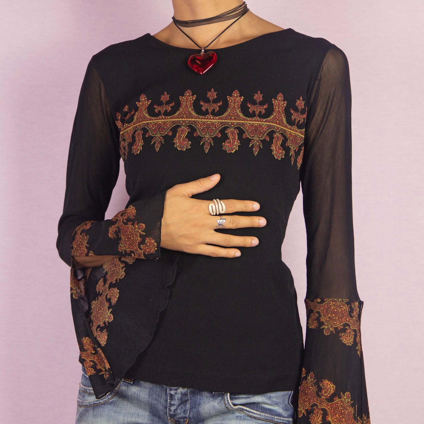 The Y2K Black Mesh Bell Sleeve Top is a vintage 2000s piece featuring a paisley-inspired print with baroque-style elements in warm hues across the chest and bell sleeves. Made from a semi-sheer mesh fabric, this top includes dramatic slit flared sleeves. Perfect for whimsical evening events.