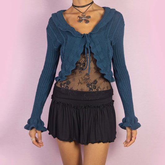 The Y2K Blue Ruffle Cropped Cardigan is a vintage 2000s romantic bolero crafted from a cozy wool blend, featuring a flattering tie-front design and playful ruffle details along the hem, sleeves, and neckline. Perfect for autumn or cooler spring days.