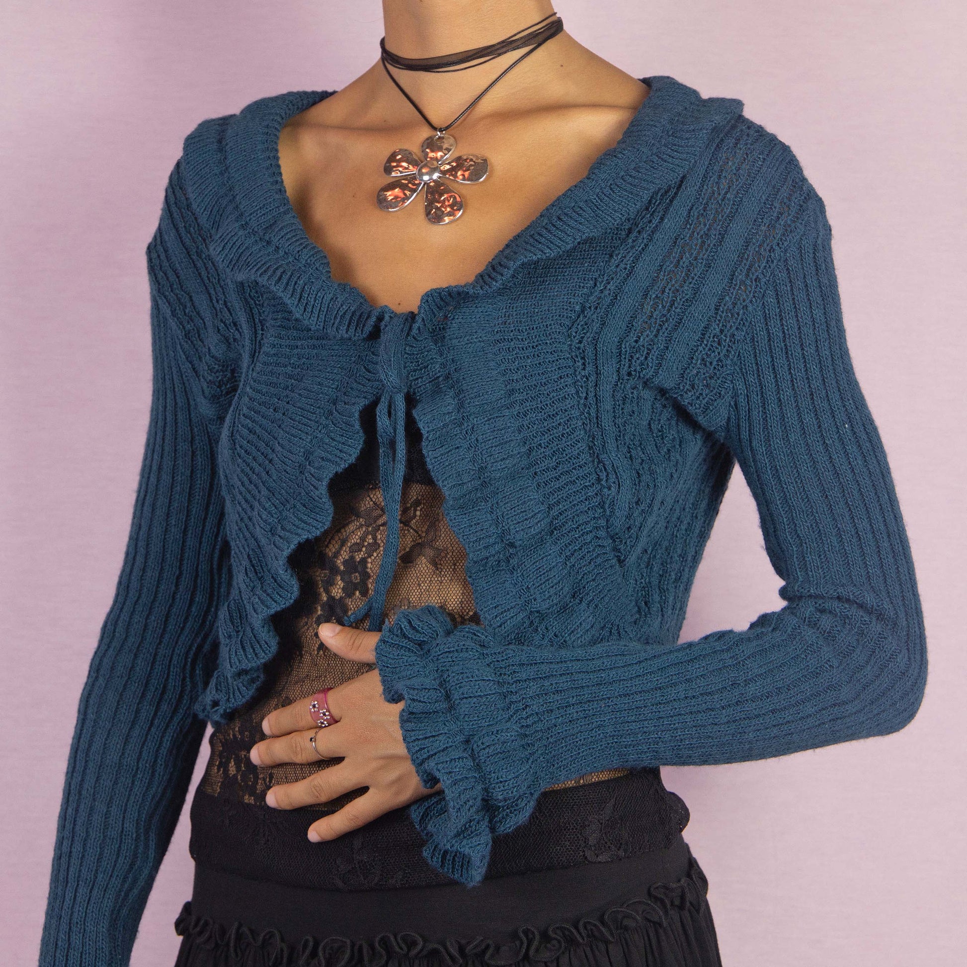 The Y2K Blue Ruffle Cropped Cardigan is a vintage 2000s romantic bolero crafted from a cozy wool blend, featuring a flattering tie-front design and playful ruffle details along the hem, sleeves, and neckline. Perfect for autumn or cooler spring days.