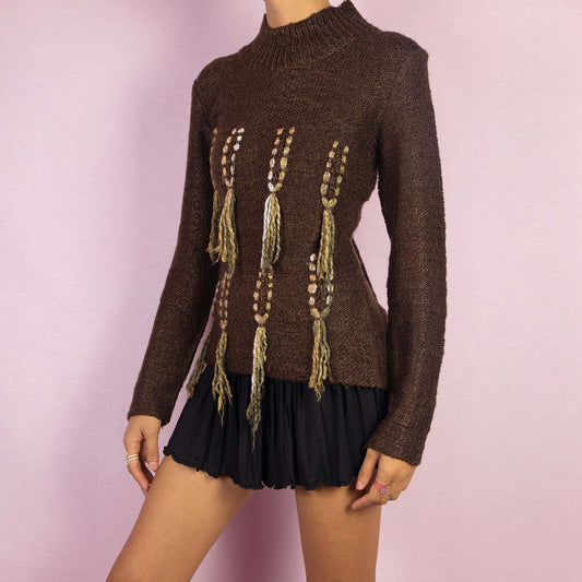 The Y2K Brown Turtleneck Sweater is a unique vintage 2000s warm pullover crafted from a cozy wool blend. It features a high turtleneck and standout embellishments with tassel details running vertically along the front. Perfect for any fall or winter wardrobe.