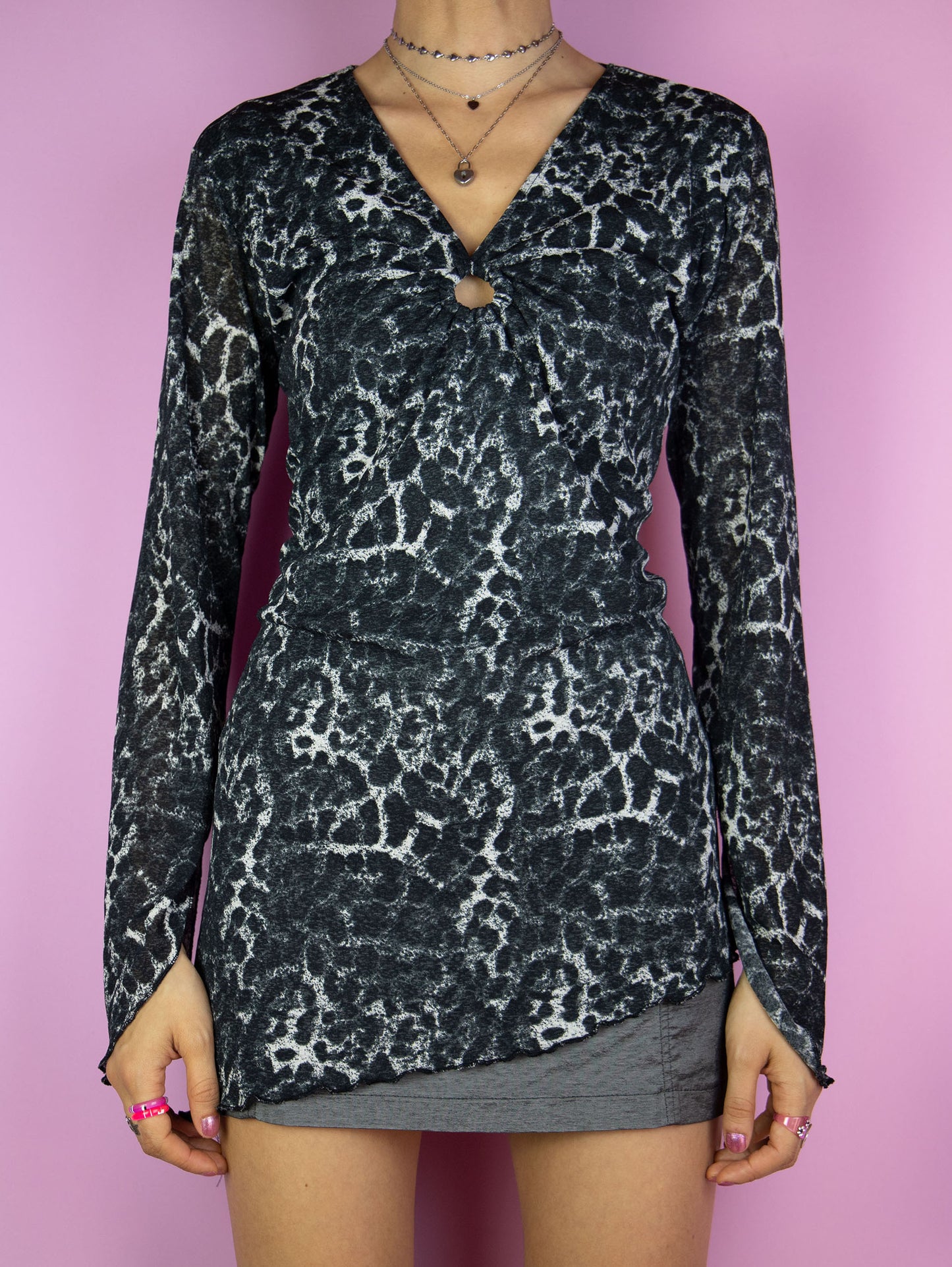 The Y2K Printed Mesh Asymmetric Top is a vintage 2000s black, gray, and white semi-sheer blouse featuring a bold leopard animal print, a ruched front with o-ring details and an asymmetric design. Perfect for any party or night out ensemble.