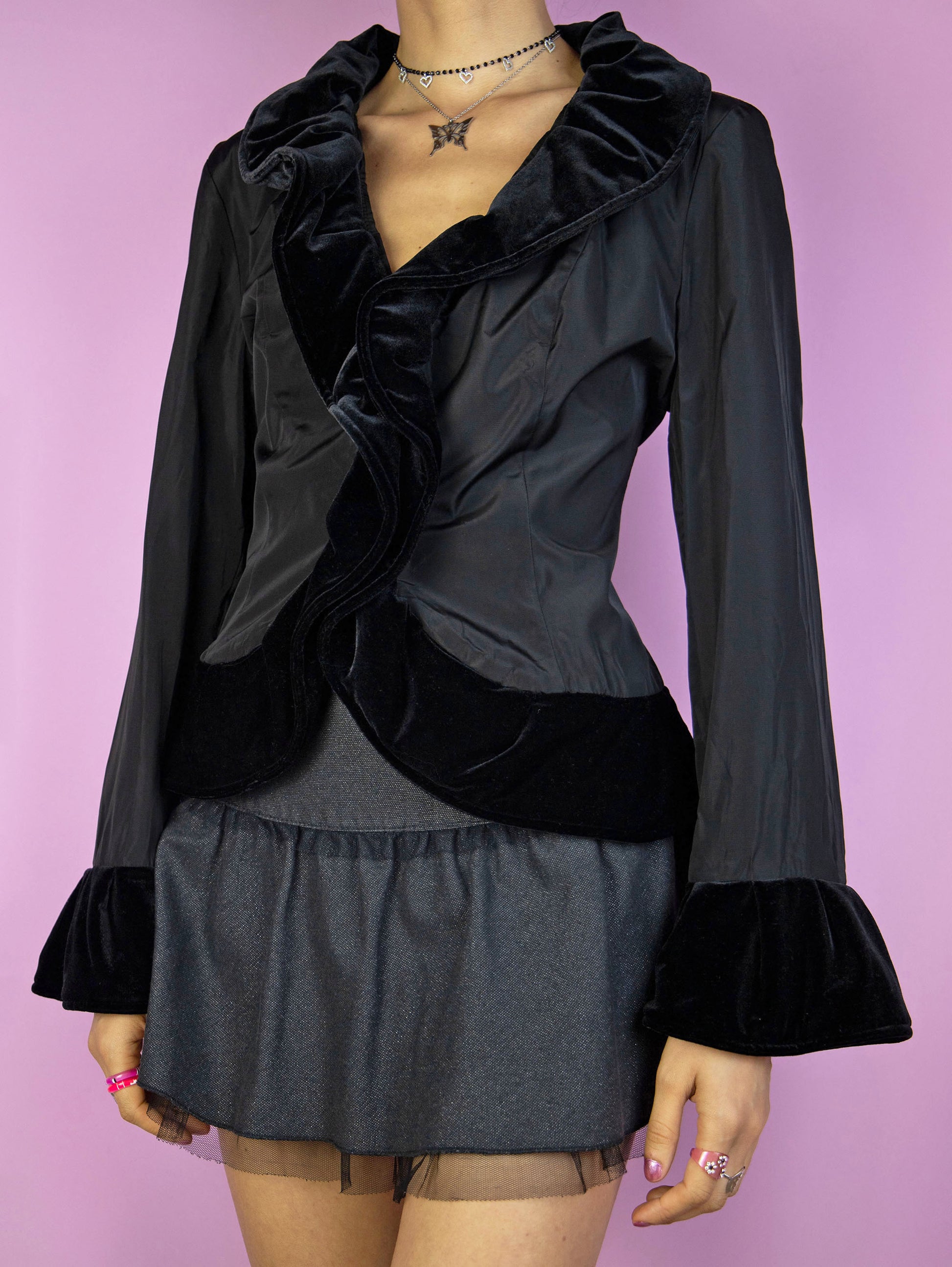 The Vintage 90s Black Ruffle Jacket is an elegant piece featuring velvet ruffles around the neckline and cuffs, along with a front hook closure. Perfect for a whimsical evening, party, or night-out outfit.