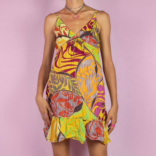 The Y2K Abstract Print Mini Dress is a vibrant vintage 2000s piece featuring a bold abstract print in bright hues of yellow, orange, purple, and green. It has a V-neckline, tie-front detail, and adjustable spaghetti straps. The dress also features a ruffled hemline. Perfect for summer parties, beach days, or casual outings.