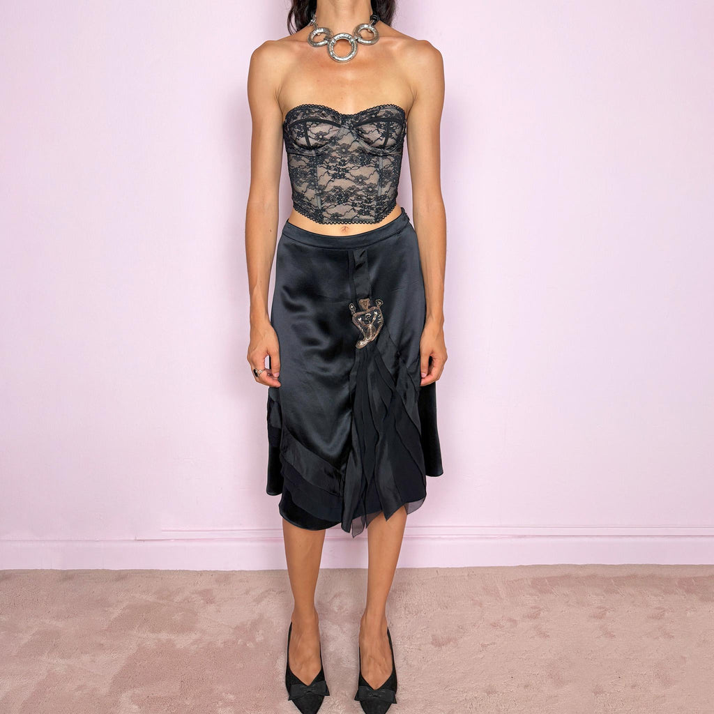 Vintage 2000s Kenzo black midi skirt crafted from 100% silk in a deep black satin finish, designed with a side zip closure and a structured no-stretch fit. It features a dramatic front detail with layered sheer pleated silk panels and an embroidered appliqué motif. A refined designer piece with a dark romantic evening feel, balancing minimal black silk with ornate Kenzo detailing. Can be worn high-waisted for size S, or slightly lower on the waist for XS and XXS. Excellent vintage condition.