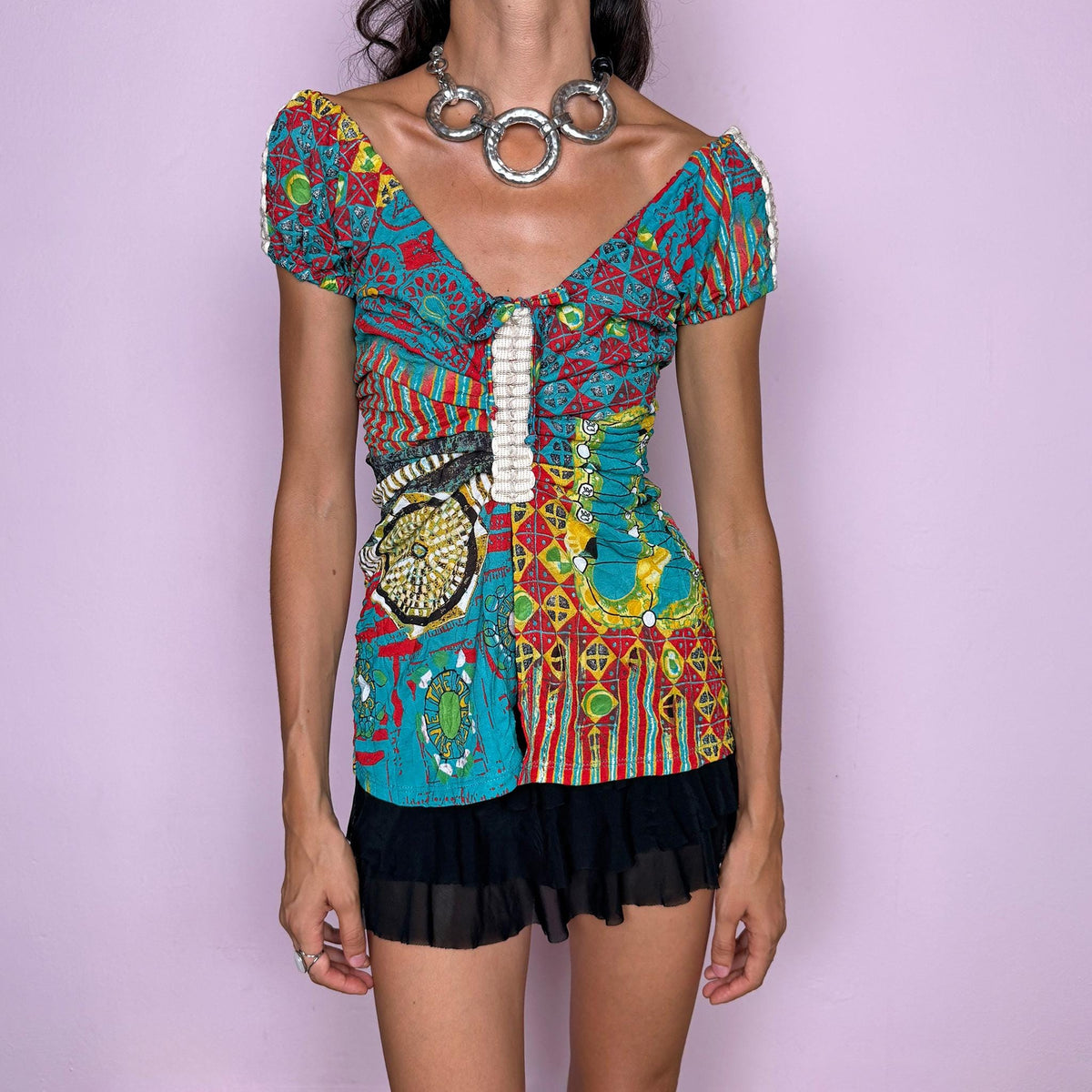 Vintage 2000s bold graphic top by Italian label Save the Queen, featuring a vivid maximalist print in turquoise, red, yellow, and green, with puffed short sleeves, a plunging V-neckline, tie-front detail, and a dramatic open split through the front. The fitted silhouette, mixed graphic motifs, and patchwork-like print give it a distinctly Y2K art-to-wear feel. Made in Italy from stretchy 100% polyester. Excellent vintage condition.