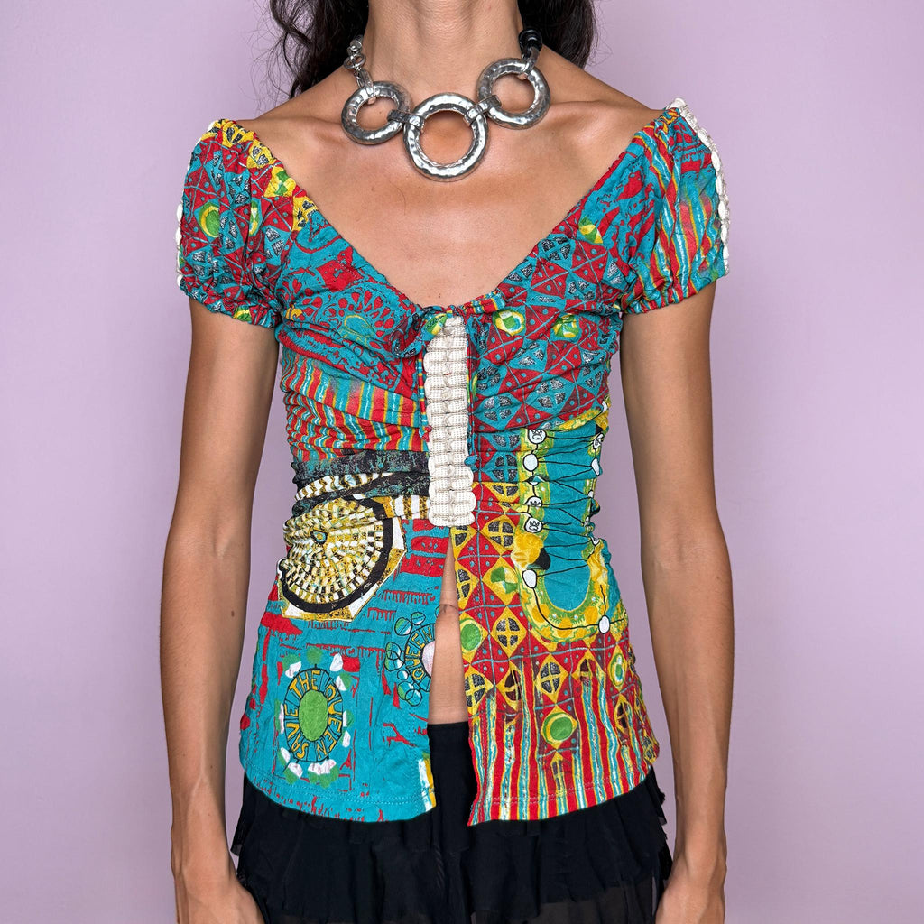 Vintage 2000s bold graphic top by Italian label Save the Queen, featuring a vivid maximalist print in turquoise, red, yellow, and green, with puffed short sleeves, a plunging V-neckline, tie-front detail, and a dramatic open split through the front. The fitted silhouette, mixed graphic motifs, and patchwork-like print give it a distinctly Y2K art-to-wear feel. Made in Italy from stretchy 100% polyester. Excellent vintage condition.