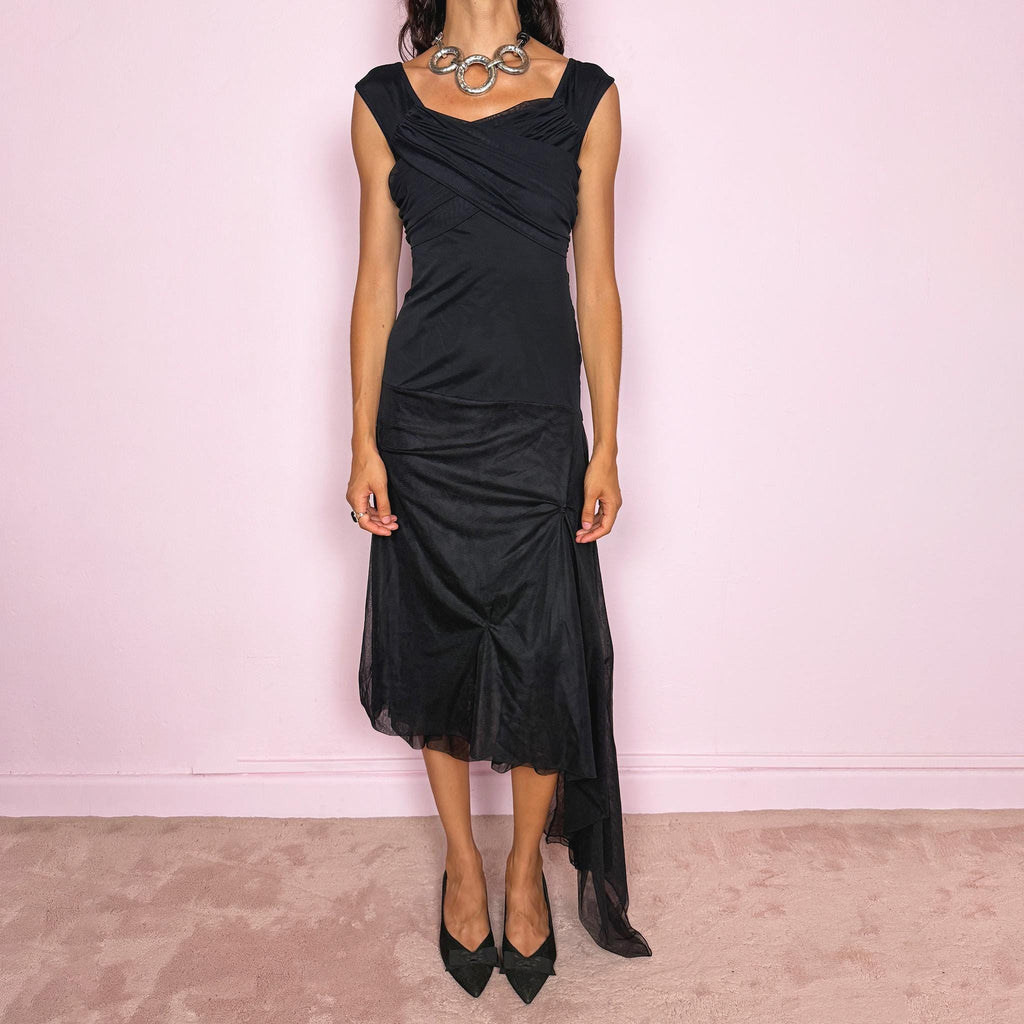 Vintage 2000s Save The Queen black midi dress with semi-sheer mesh layering and a sculptural asymmetric silhouette. It features a softly draped off-shoulder neckline, short cap sleeves, a fitted stretch body with diagonal ruching through the bust and waist, and an asymmetric layered skirt with sheer mesh panels, gathered details, and a long cascading side drape for dramatic movement. A rare Italian Y2K statement piece with a dark romantic evening feel, perfect for elegant parties and occasions.