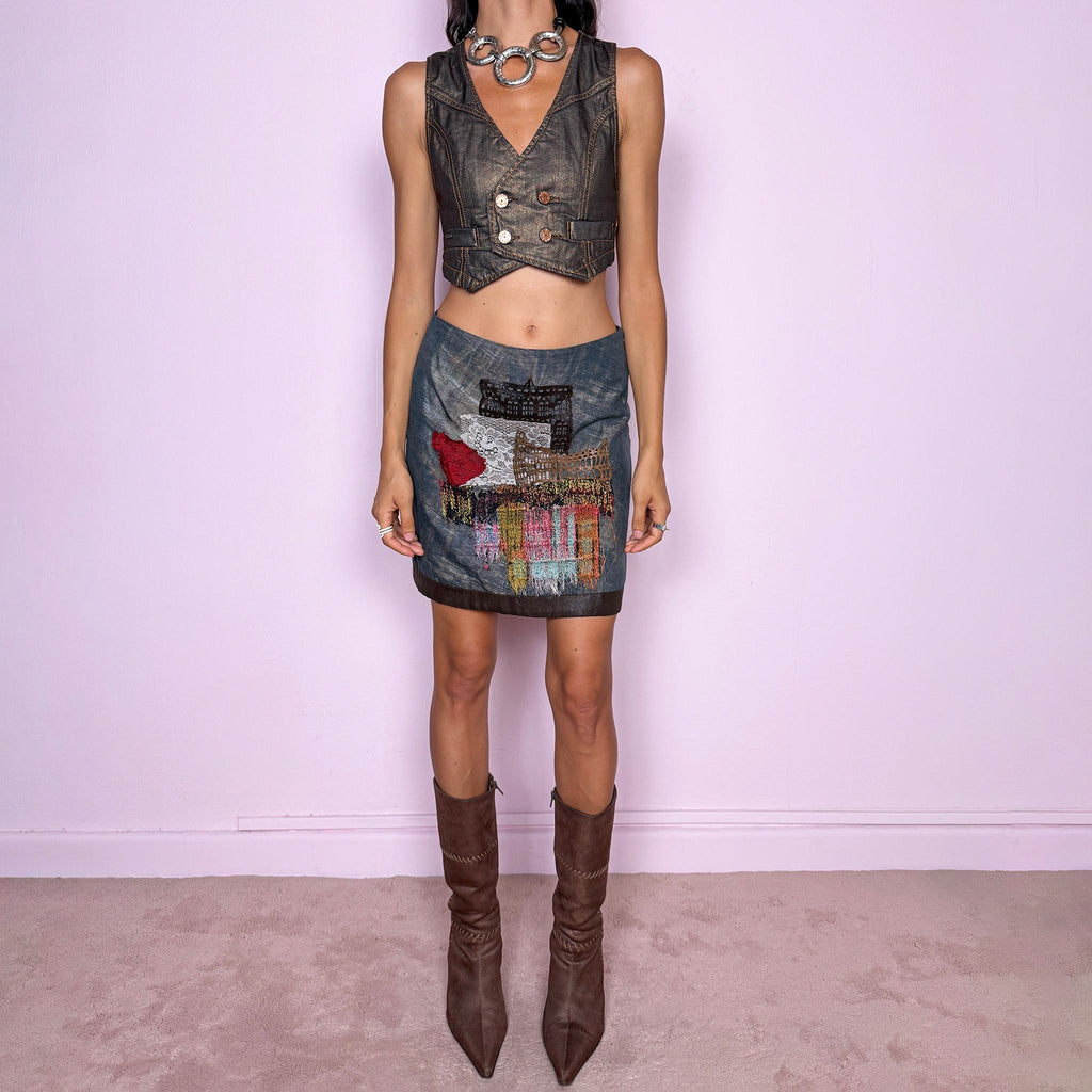 Vintage 2000s art-to-wear mini skirt by Italian label Save the Queen, made in Italy from a structured 70% wool and 30% polyester blend. Features a muted blue-gray base with iridescent gold-beige tones and an elaborate mixed-media appliqué composition across the front, combining lace, textured threads, frayed woven panels, and architectural-inspired motifs. Designed with a fitted, straight silhouette and side zip closure. Non-stretch. The handcrafted collage effect gives it an avant-garde