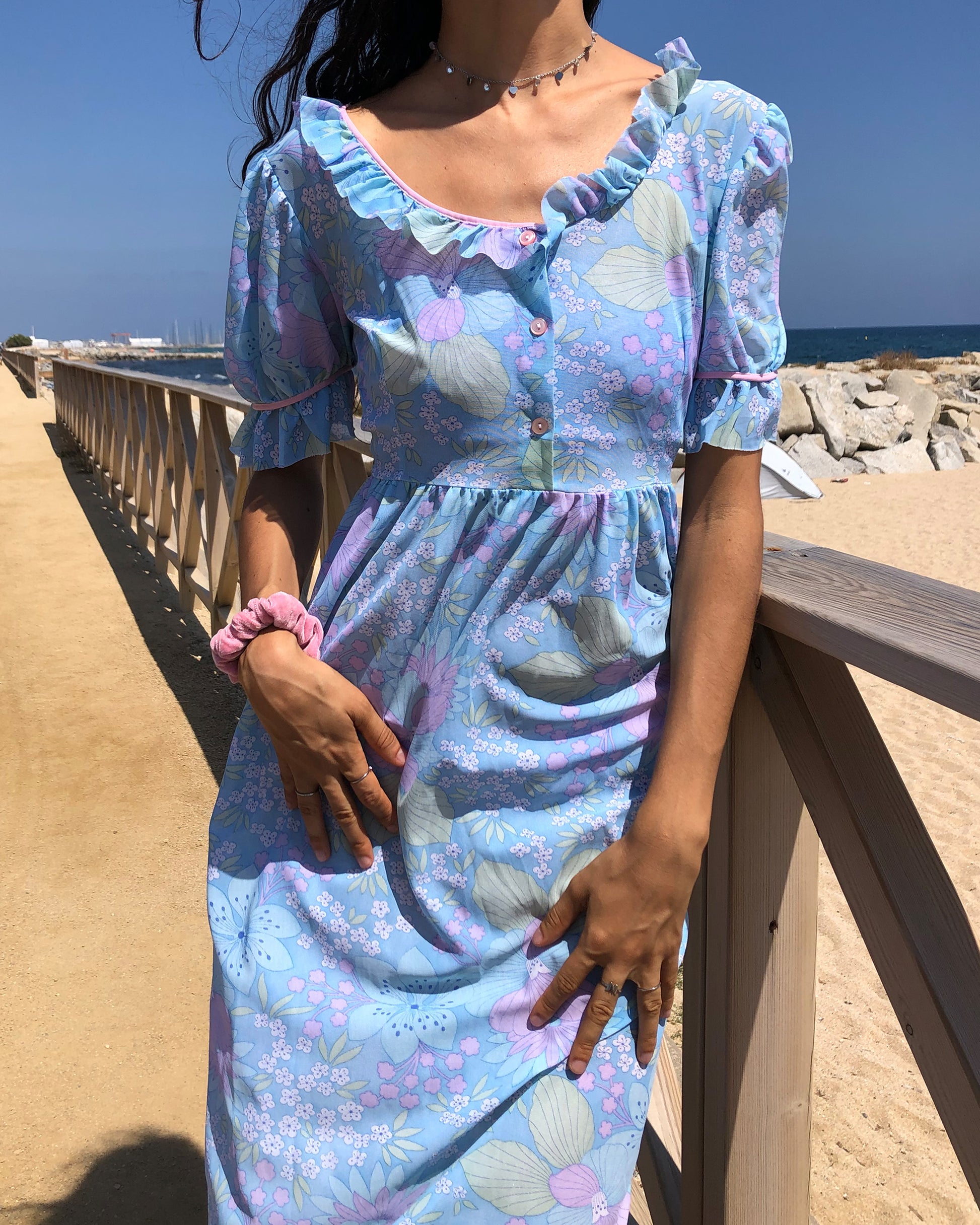 This vintage 1970s blue floral midi dress features lightweight semi-sheer fabric in soft pastel tones with a square neckline and ruffle trim, puff sleeves with frilled cuffs, and a button-front bodice. The empire waist and flowing length create gentle prairie romance for spring picnics, cottagecore styling, or feminine nostalgia. Made in France from a polyamide nylon blend. Excellent vintage condition.