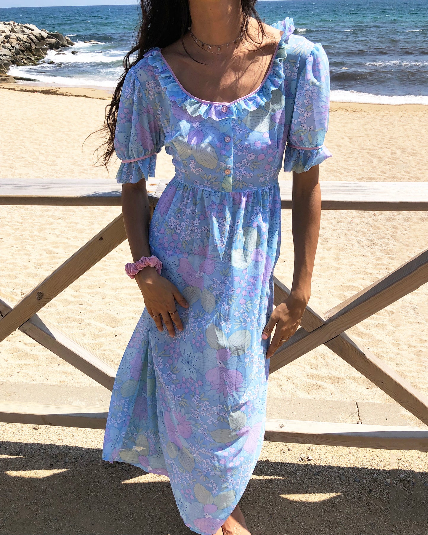 This vintage 1970s blue floral midi dress features lightweight semi-sheer fabric in soft pastel tones with a square neckline and ruffle trim, puff sleeves with frilled cuffs, and a button-front bodice. The empire waist and flowing length create gentle prairie romance for spring picnics, cottagecore styling, or feminine nostalgia. Made in France from a polyamide nylon blend. Excellent vintage condition.