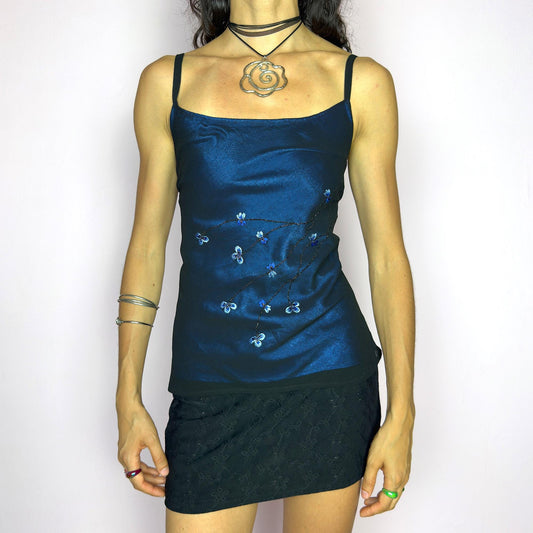 This vintage 90s black cami top features a delicate semi-sheer overlay with ethereal blue floral embroidery. Designed with a soft satin-style underlayer and subtle shimmer, it offers a flattering fit. Romantic and versatile, perfect for weddings, cocktail parties, or evening events. A dreamy, feminine piece that blends elegance with quiet charm. Excellent vintage condition.