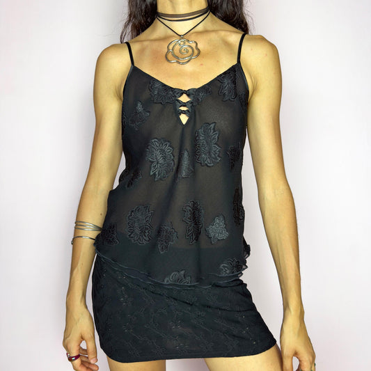 This vintage 90s black cami top features sheer fabric with tonal floral appliqué embroidery and a delicate keyhole neckline adorned with tiny bows. Designed with adjustable spaghetti straps and a soft flared hem, it drapes effortlessly over the body. Lightweight and breathable, it’s ideal for summer cocktail nights, romantic layering, or lounge styling. Feminine, elegant, and quietly seductive. Great vintage condition.