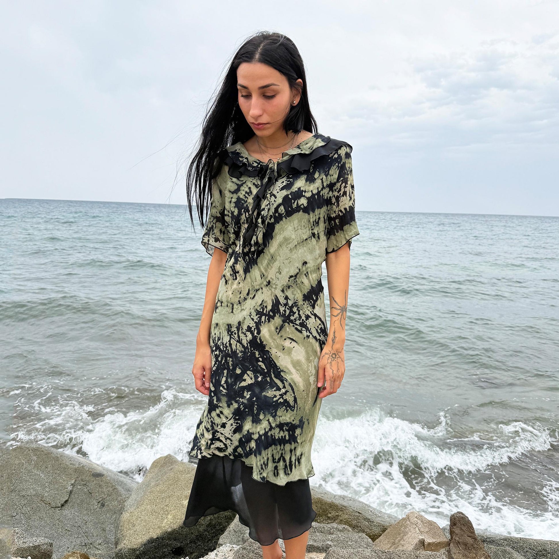 This vintage 90s midi dress features a black and green tie-dye pattern with a ruffled neckline. The short sleeves and flowy layered hem make it ideal for summer festivals, boho gatherings, or dark fairy-inspired looks. A unique Italian-made piece, perfect for forest parties or artistic styling. Made in Italy from lightweight non-stretch fabric. Excellent vintage condition.