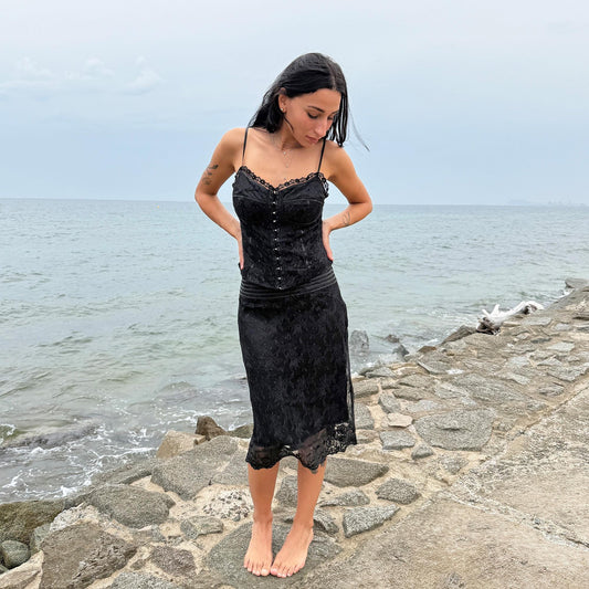 This vintage 90s two-piece set features a black lace corset-style top with hook front closure, light boning, and structured cups, making it especially suited for a fuller bust. Paired with a black lace midi skirt featuring sequin trim at the hem and side zipper closure. A romantic goth statement, perfect for cocktail, evening, or formal wear. Rare archival matching set. Great vintage condition.