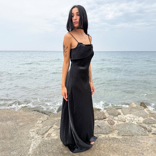 This vintage 90s slip dress in black features a lustrous finish with a straight, folded neckline and subtle ruched detailing. The fitted silhouette extends into a sleek midi length with a side zipper closure, making it ideal for evening galas, cocktail parties, or formal occasions. A stunning dark romance piece—timeless and elegant. Made from non-stretch fabric with a soft sheen. Great vintage condition.