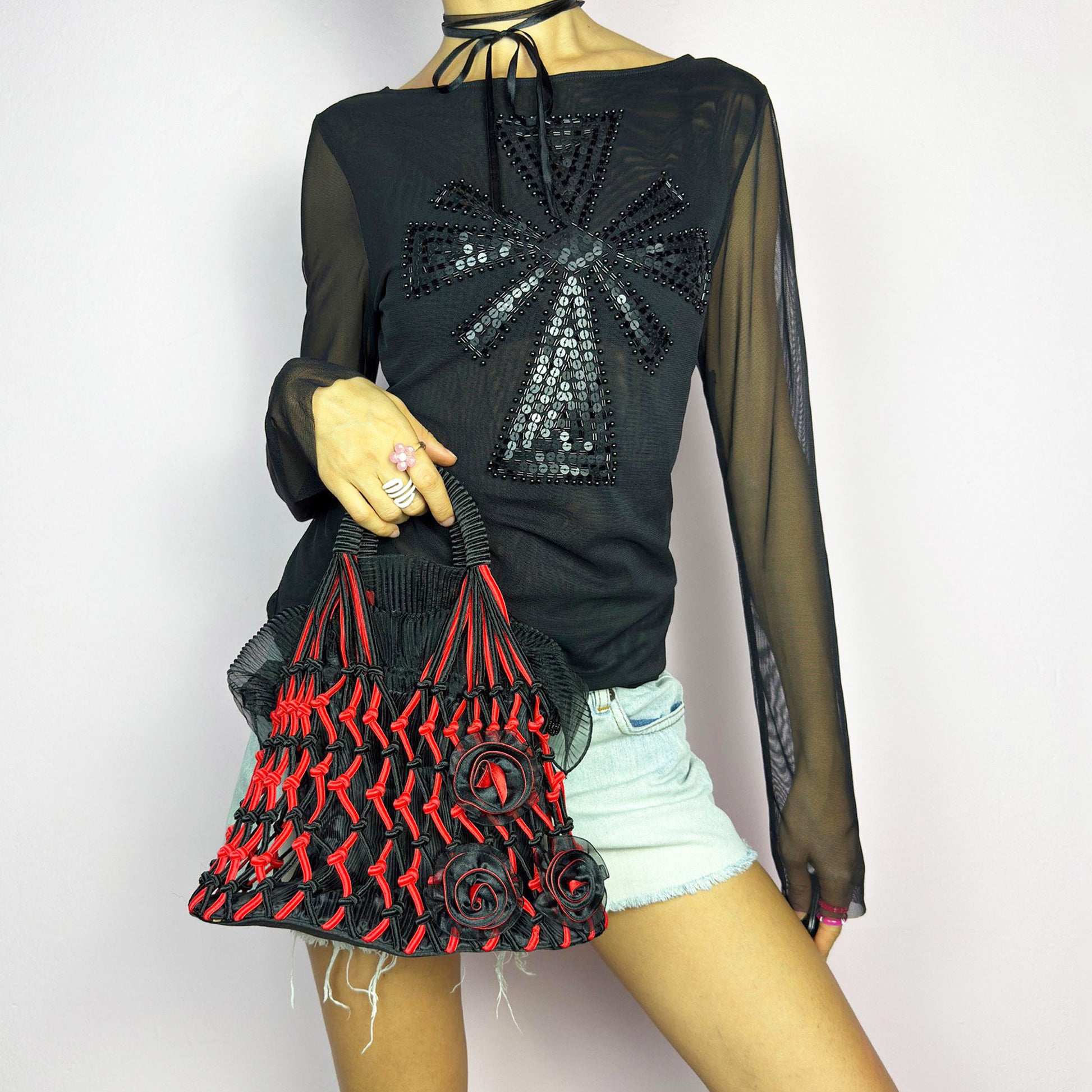 The Vintage 90s Top Handle Drawstring Bag is a unique statement accessory. It features a striking black and red woven design with intricate knot details and decorative rosettes. The semi-structured shape includes a soft, pleated fabric drawstring closure. Perfect for bold artistic outfits. Great vintage condition.