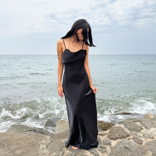 This vintage 90s slip dress in black features a lustrous finish with a straight, folded neckline and subtle ruched detailing. The fitted silhouette extends into a sleek midi length with a side zipper closure, making it ideal for evening galas, cocktail parties, or formal occasions. A stunning dark romance piece—timeless and elegant. Made from non-stretch fabric with a soft sheen. Great vintage condition.