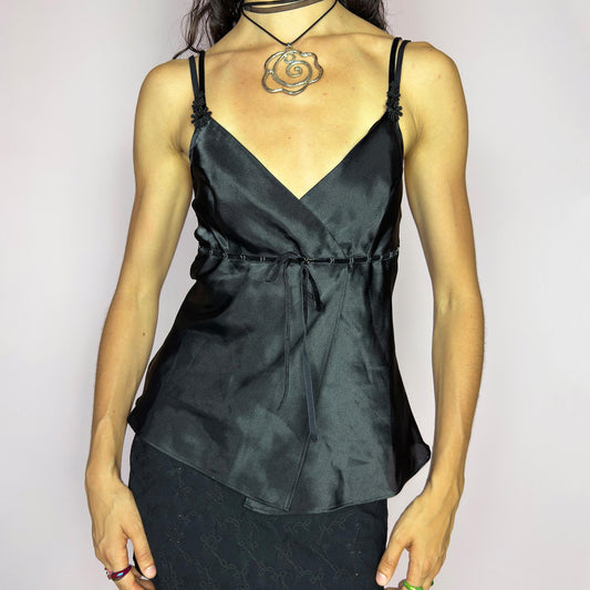 This vintage 90s black satin-style cami top features a wrap front silhouette with a subtle tie at the waist, adding gentle structure to its soft drape. Finished with delicate floral appliqués and adjustable double spaghetti straps, it captures a mood of refined sensuality. Perfect for cocktail nights, evening events, or romantic layering. Lightweight and fluid, it brings feminine elegance with a hint of 90s glamour. Excellent vintage condition.