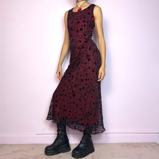 The Vintage 90s Black Sheer Floral Midi Dress is a striking piece featuring a sheer black overlay with textured velvet floral details layered over a vibrant red lining. The sleeveless design and round neckline offer a timeless silhouette, while the fitted shape and midi length create a flattering, romantic look. The fabric is slightly stretchy and flowy, with a gothic romantic vibe perfect for dark fairycore, witchy looks, or 2000s party aesthetics. Excellent vintage condition.