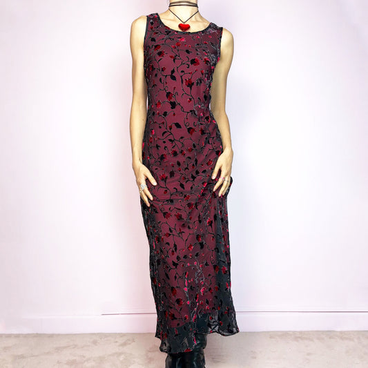 The Vintage 90s Black Sheer Floral Midi Dress is a striking piece featuring a sheer black overlay with textured velvet floral details layered over a vibrant red lining. The sleeveless design and round neckline offer a timeless silhouette, while the fitted shape and midi length create a flattering, romantic look. The fabric is slightly stretchy and flowy, with a gothic romantic vibe perfect for dark fairycore, witchy looks, or 2000s party aesthetics. Excellent vintage condition.