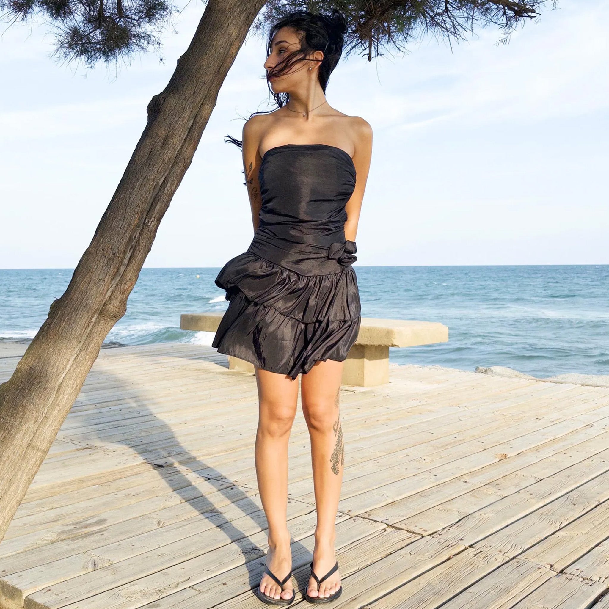 Vintage 90s black mini dress with a sculptural strapless shape, ruched draping and voluminous double ruffle tiers. Features a tie-back, shirred elastic back panel and side zip. Ideal for summer nights, cocktail events or rooftop parties. Made in Italy from a polyester blend. Excellent vintage condition.