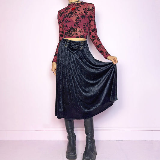 The Vintage 90s Black Velvet Midi Skirt is crafted from soft velvet and features an elastic waistband detail with button accents and a flowing A-line silhouette. Ideal for night parties and embodies a whimsical goth aesthetic. Great vintage condition.