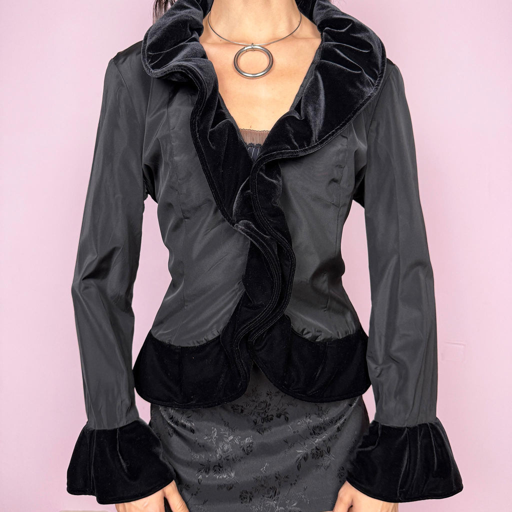 Dark romance vintage 90s lightweight formal black jacket with dramatic bell sleeves and ruffled cuffs. Features a ruffled neckline trimmed in black velvet and a front hook closure. Structured silhouette with no stretch, ideal for gala events, elegant evening parties, or Victorian goth styling. Made by a European brand. Excellent vintage condition.