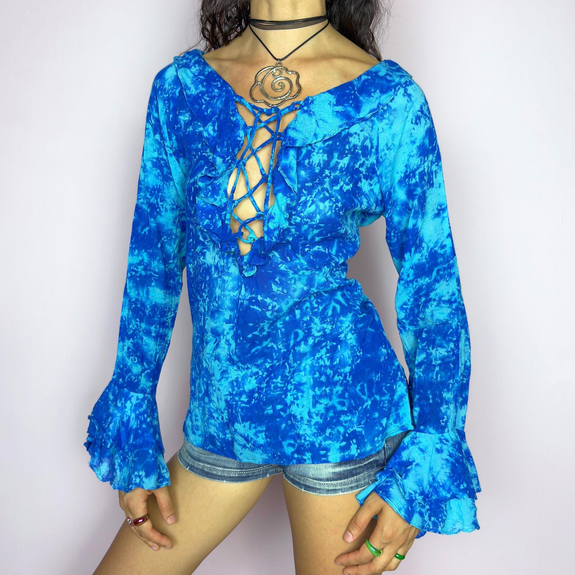This vintage 90s blue tie dye top features dramatic ruffle cuffs, a deep lace-up neckline, and soft cotton-blend fabric in vibrant psychedelic tones. Designed with long sleeves it channels boho, hippie, and festival energy with bold originality. Lightweight and breathable, perfect for summer layering or statement styling. A rare archival blouse that captures wild 90s freedom. Excellent vintage condition.