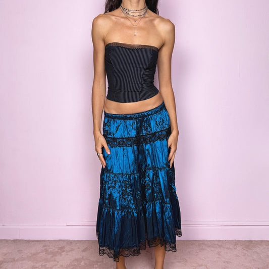 This stunning vintage 90s blue tiered midi skirt features an elastic waist, black lace trims, and delicate applique details for a dreamy, gothic silhouette. The rich sheen and romantic texture evoke dark romance and witchy elegance, perfect for formal nights, parties, or galas. Fits low-rise or high-rise for XS and S sizes. Excellent vintage condition.