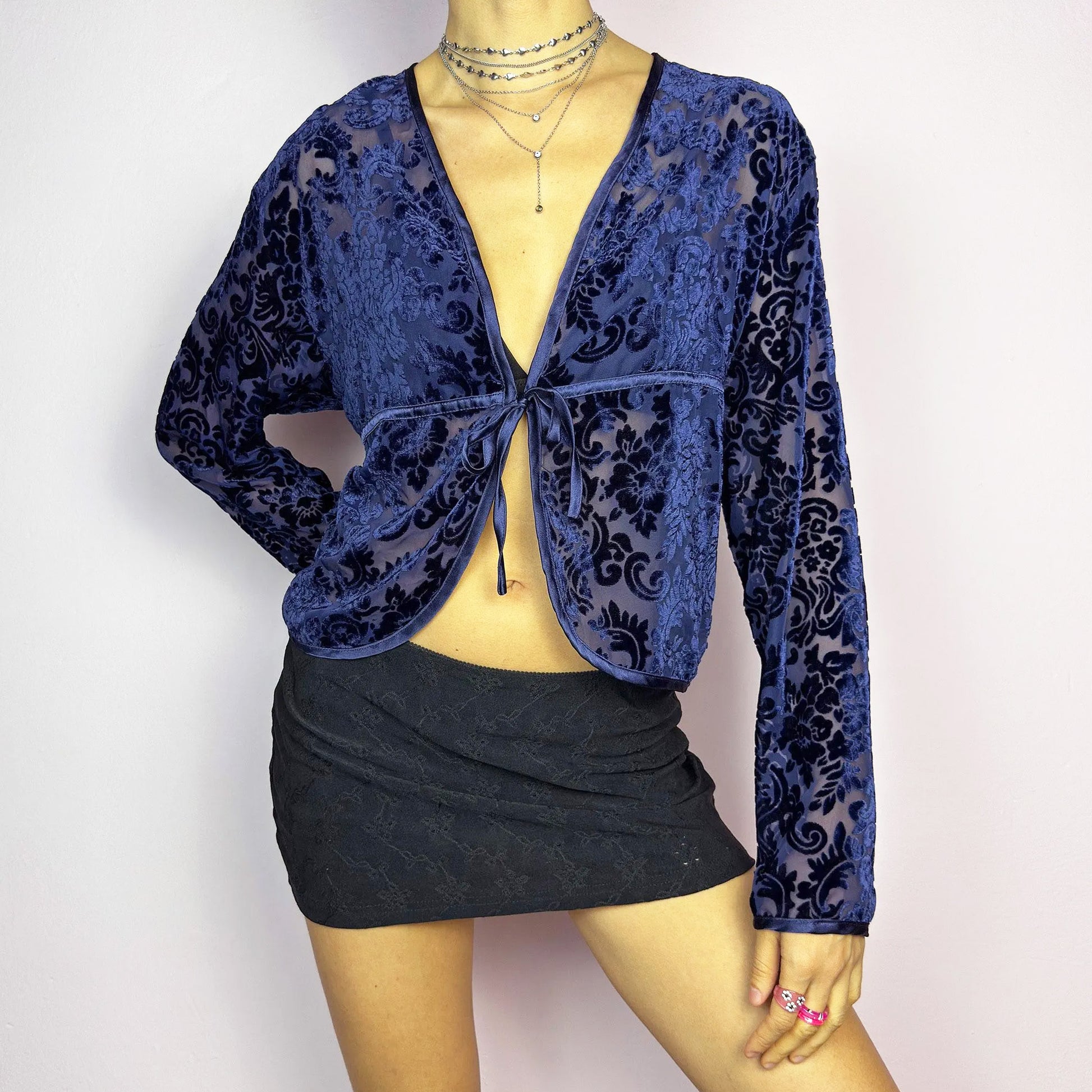 This vintage 90s blue devore velvet blouse features a sheer finish with a flocked baroque floral pattern in deep navy tones. Designed with a V-neckline, long sleeves, and a delicate tie-front closure, it radiates romantic allure, perfect for night-out or evening layering. A sensual and timeless vintage piece. Excellent vintage condition.
