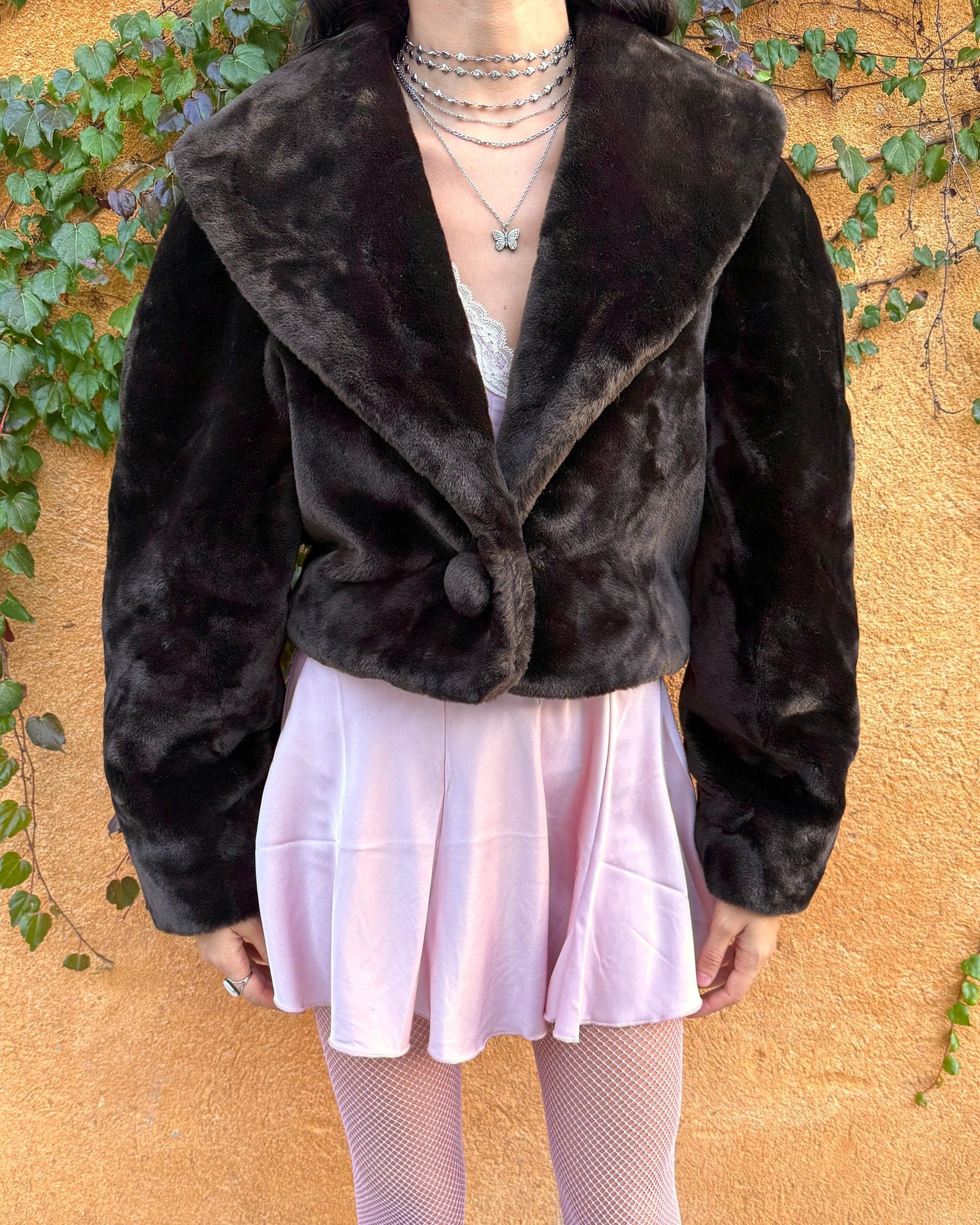 Vintage 90s dark brown faux fur cropped jacket featuring an exaggerated wide collar and a single hook-button closure. Soft, plush, and luxurious, it adds instant elegance to formal winter outfits and is perfect for gala events, prom nights, or refined evening layering. The cropped cut balances the dramatic collar, creating a chic silhouette that elevates dresses or slip styles with minimal effort. Made in Spain. Excellent vintage condition.