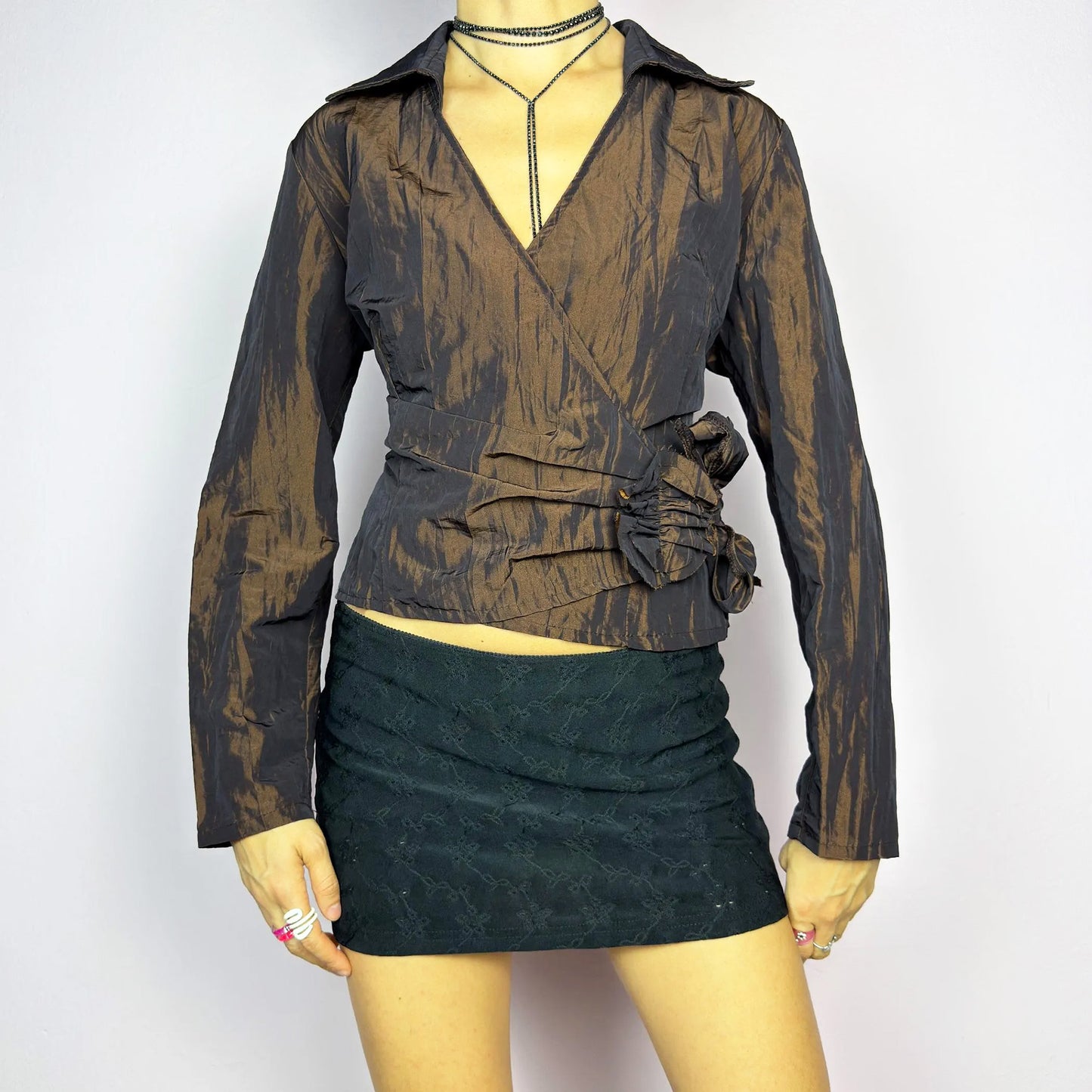 The Vintage 90s Brown Wrap Tie Blouse features a textured, crinkled fabric with a subtle iridescent finish, a flattering wrap design with a tie at the side. The deep brown tone adds versatility, while the structured collar and long sleeves give it a chic, tailored look. Perfect for evening occasions or adding a touch of glamour to casual outfits. Excellent vintage condition.