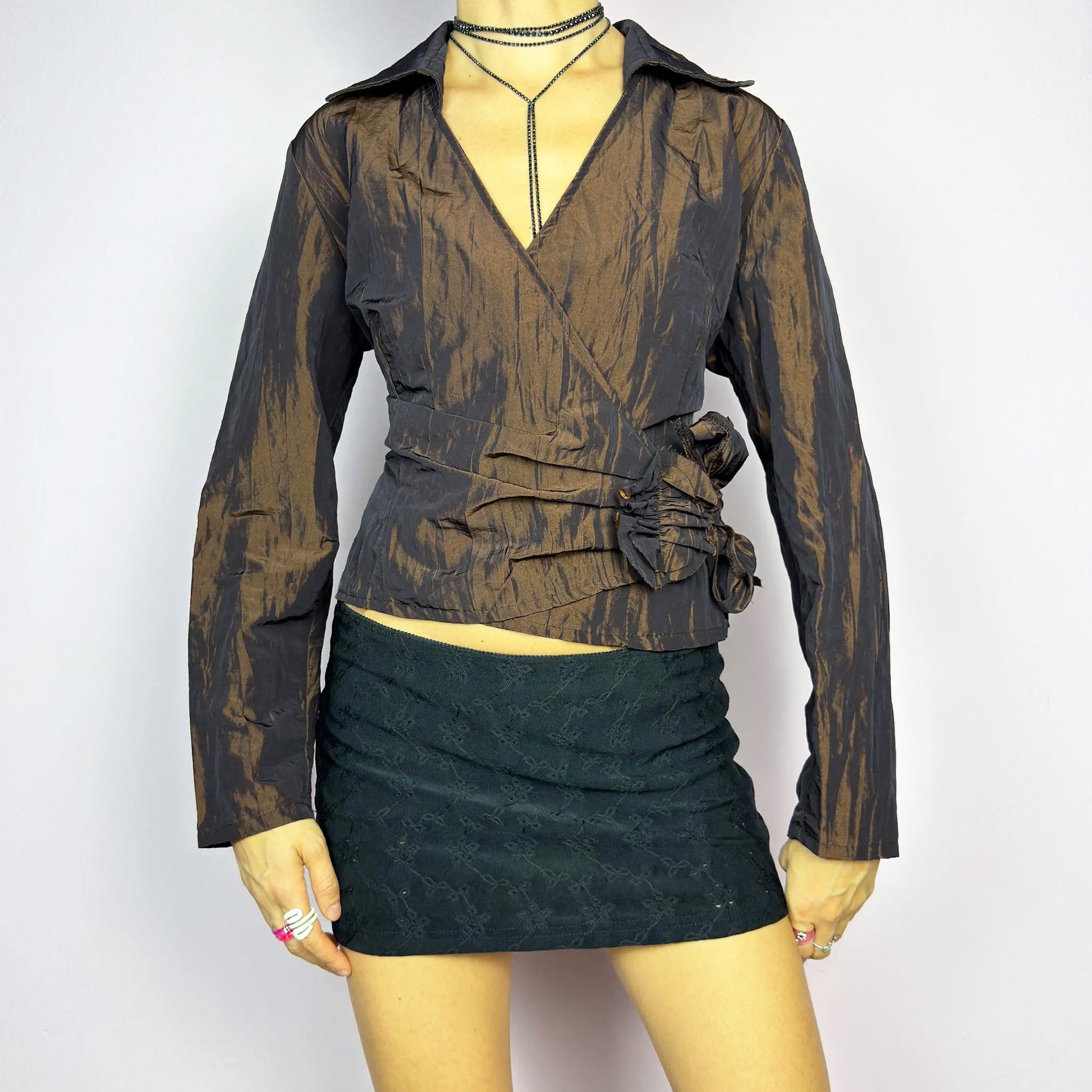 The Vintage 90s Brown Wrap Tie Blouse features a textured, crinkled fabric with a subtle iridescent finish, a flattering wrap design with a tie at the side. The deep brown tone adds versatility, while the structured collar and long sleeves give it a chic, tailored look. Perfect for evening occasions or adding a touch of glamour to casual outfits. Excellent vintage condition.