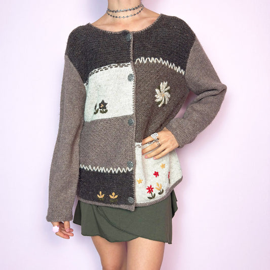 The Vintage 90s Brown Patchwork Cardigan features a cozy wool and acrylic blend in earthy brown tones, with whimsical floral embroidery and decorative stitching. The patchwork layout and traditional edelweiss-style metal buttons add a folk-inspired, alpine feel, reminiscent of handmade knits from mountain villages. Soft, warm, and full of character—perfect for layering in colder seasons or styling with cottagecore and fairycore outfits. Great vintage condition.
