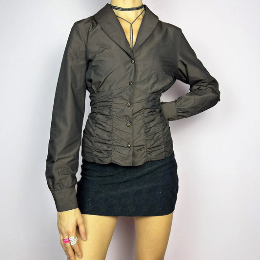 The Vintage 90s Brown Ruched Blouse features a structured yet feminine design with ruched detailing on both the front and back, creating a flattering silhouette. Crafted in a deep brown tone, it includes a tailored collar, long sleeves with buttoned cuffs, and a button-down closure. Perfect for both formal occasions and chic everyday styling. Excellent vintage condition.