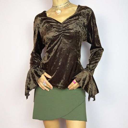 The Vintage 90s Brown Velvet Top is an elegant piece crafted from soft, stretchy velvet fabric. It features a rich chocolate brown hue, a flattering V-neckline with ruching detail at the bust, and dramatic bell sleeves. Perfect for whimsy evening wear. Excellent vintage condition.