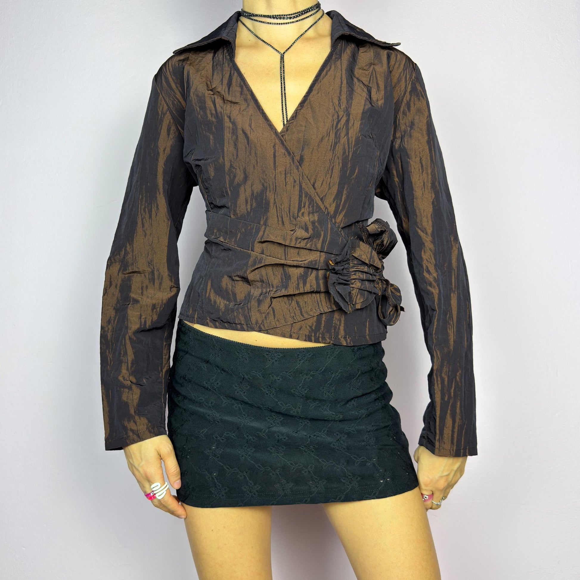 The Vintage 90s Brown Wrap Tie Blouse features a textured, crinkled fabric with a subtle iridescent finish, a flattering wrap design with a tie at the side. The deep brown tone adds versatility, while the structured collar. adult world shop