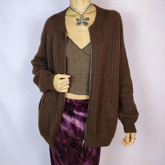 The Vintage 90s Brown Zip Cardigan features a relaxed fit with a ribbed knit design, full front zipper closure, and two pockets for a functional yet cozy style. Crafted in a dark warm brown tone, this versatile piece is perfect for layering