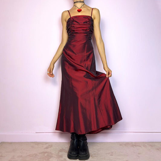 The Vintage 90s Burgundy Ruched Maxi Dress is a show-stopping piece featuring a rich burgundy tone with a lustrous satin-style finish. The ruched bodice adds texture and dimension, while the fitted silhouette flows into a soft A-line skirt. Designed with dainty spaghetti straps, a maxi length for dramatic flair, and a hidden side zipper closure for a seamless fit. Perfect for prom, formal events, or romantic night-outs. Excellent vintage condition.