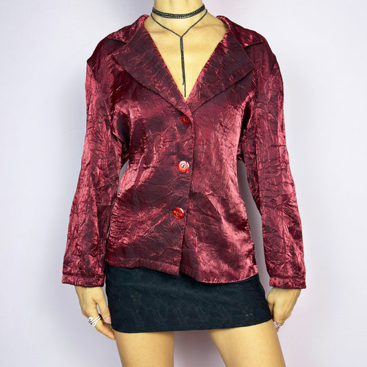 The Vintage 90s Red Iridescent Jacket is a striking and glamorous piece featuring a textured, crinkled design with a luxurious, iridescent sheen. This button-up jacket showcases a deep red tone, wide lapels, and bold red buttons for a dramatic look. Perfect for evening outings or as a statement piece to elevate your outfit. Excellent vintage condition.
