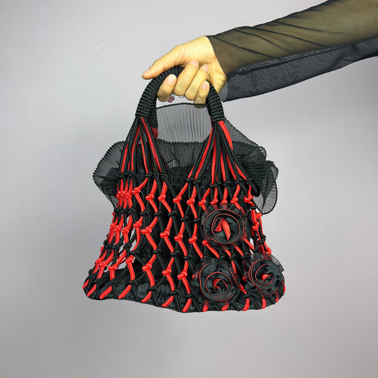 The Vintage 90s Top Handle Drawstring Bag is a unique statement accessory. It features a striking black and red woven design with intricate knot details and decorative rosettes. The semi-structured shape includes a soft. adult world shop