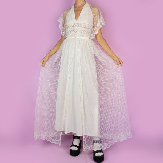 The Vintage 90s White Sheer Duster is a dreamy and ethereal robe, featuring a sheer polka-dot overlay with delicate lace detailing along the edges. The flowy silhouette, flutter sleeves, and maxi length add a romantic charm. Adult World Shop
